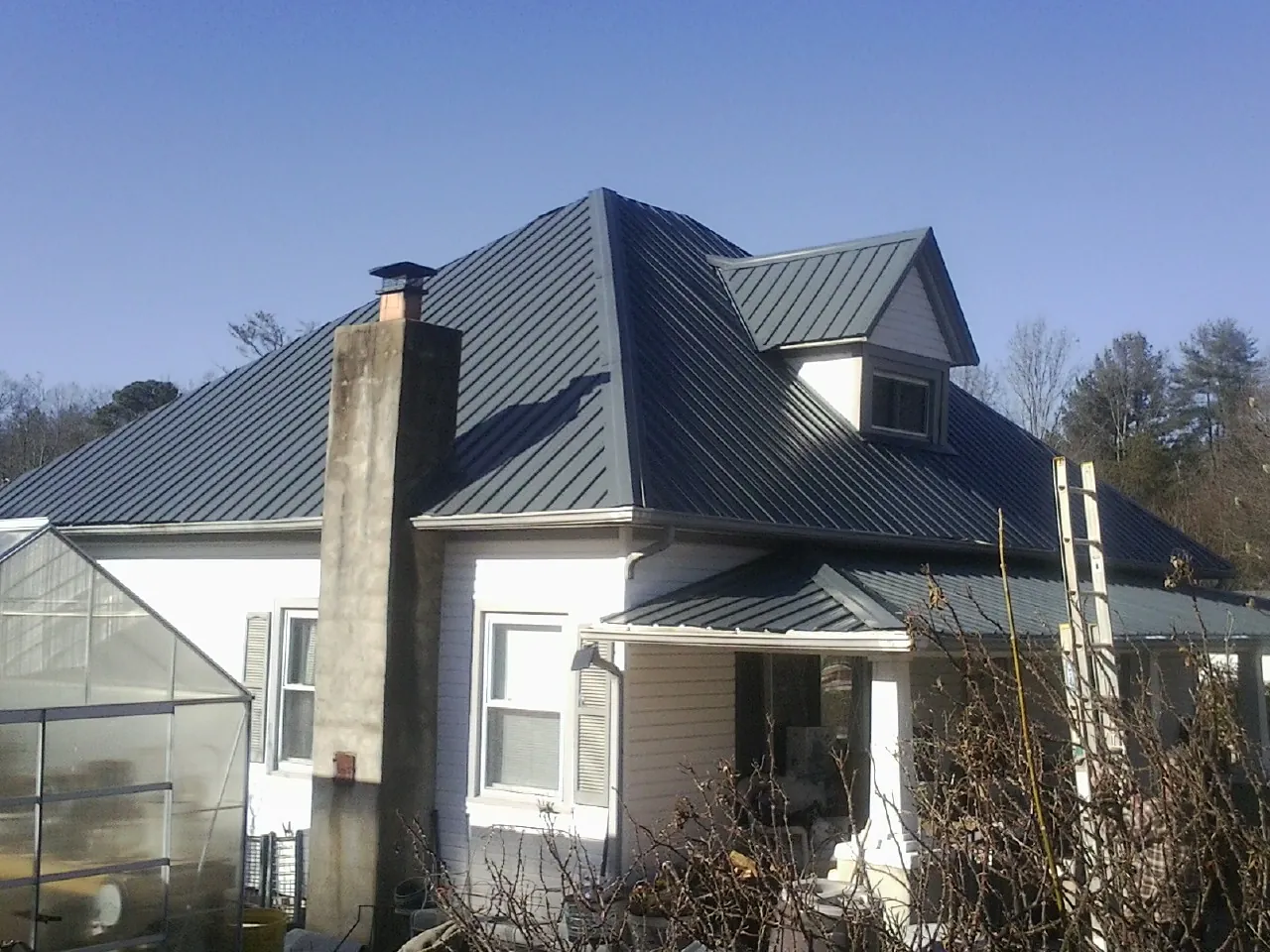 Dark blue standing seam metal roof on a white farmhouse with dormer — Slate & Tile Roof Repair by Roofing Brothers in Blue Springs