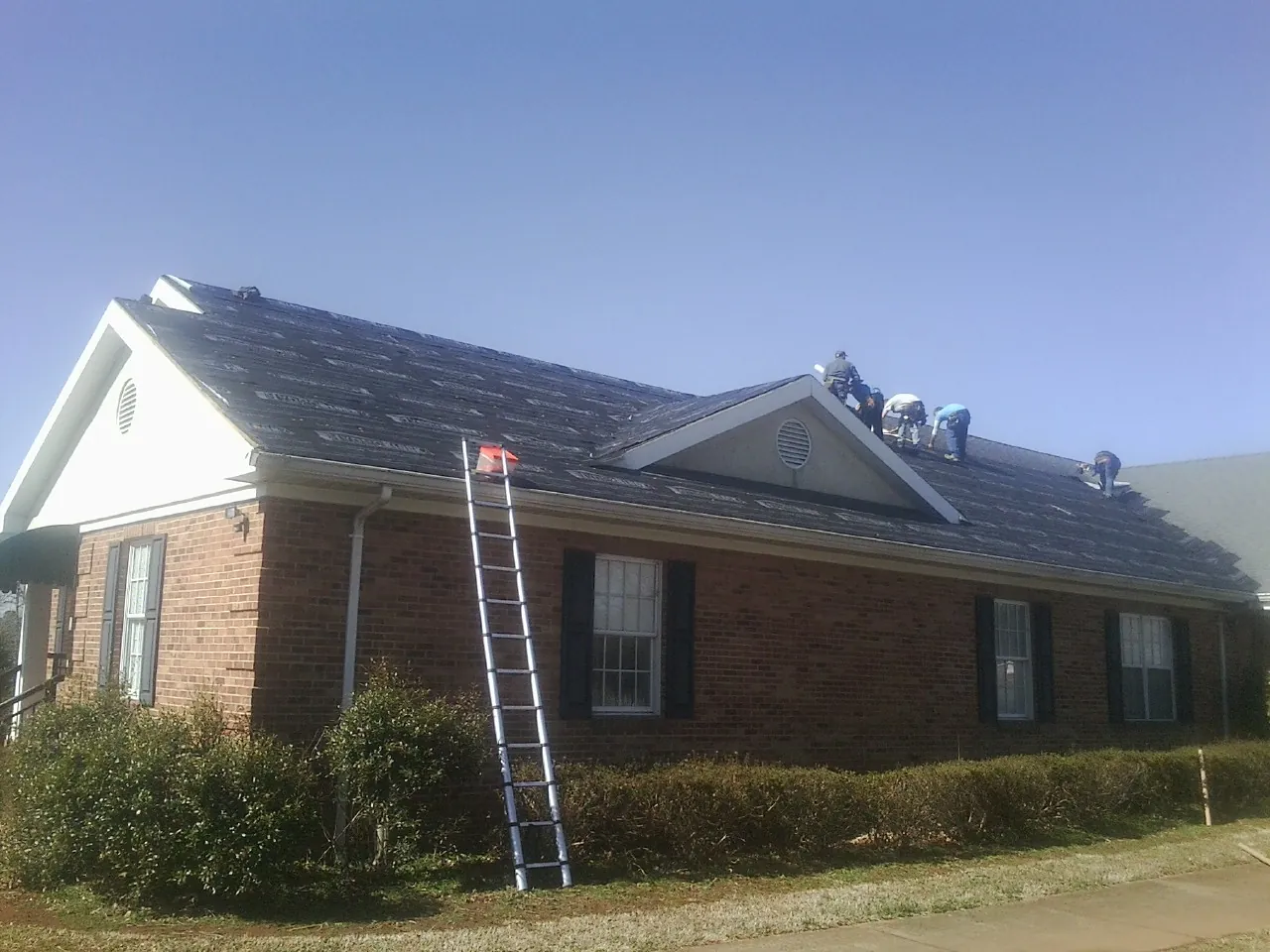 Crew tearing shingles off a brick ranch roof with a ladder set — Metal Roof Repair work by our crew in Blue Springs