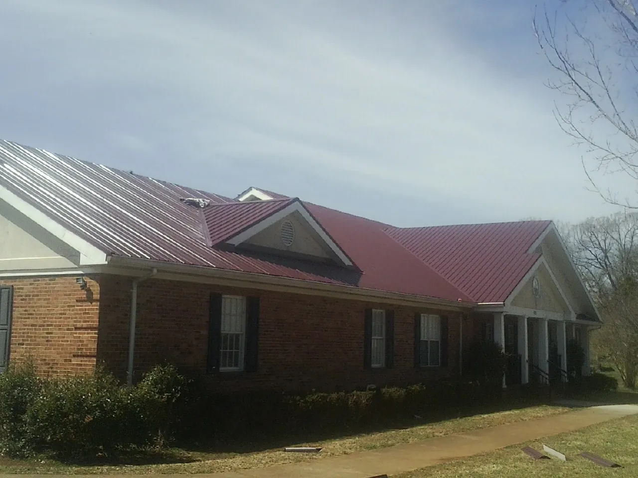 Red metal roof with gabled entries on a long brick building, from a Hail Damage Roof Repair job in Blue Springs