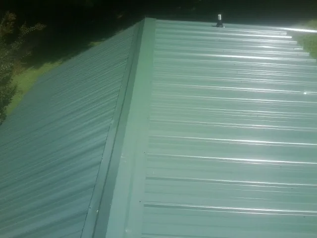 New green metal panels meeting at the ridge of a roof — Flat Roof Repair work by our crew in Blue Springs