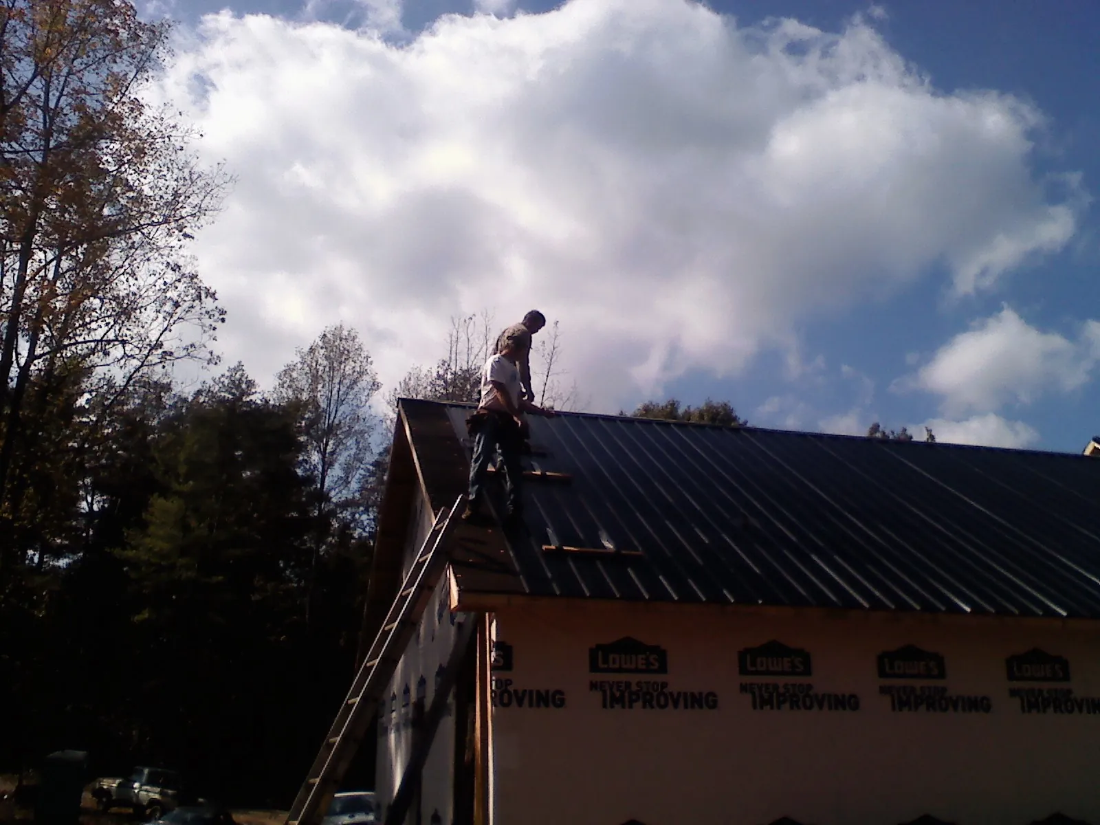 Roofer fastening dark metal panels high against a cloudy sky, from a Roof Inspection job in Blue Springs