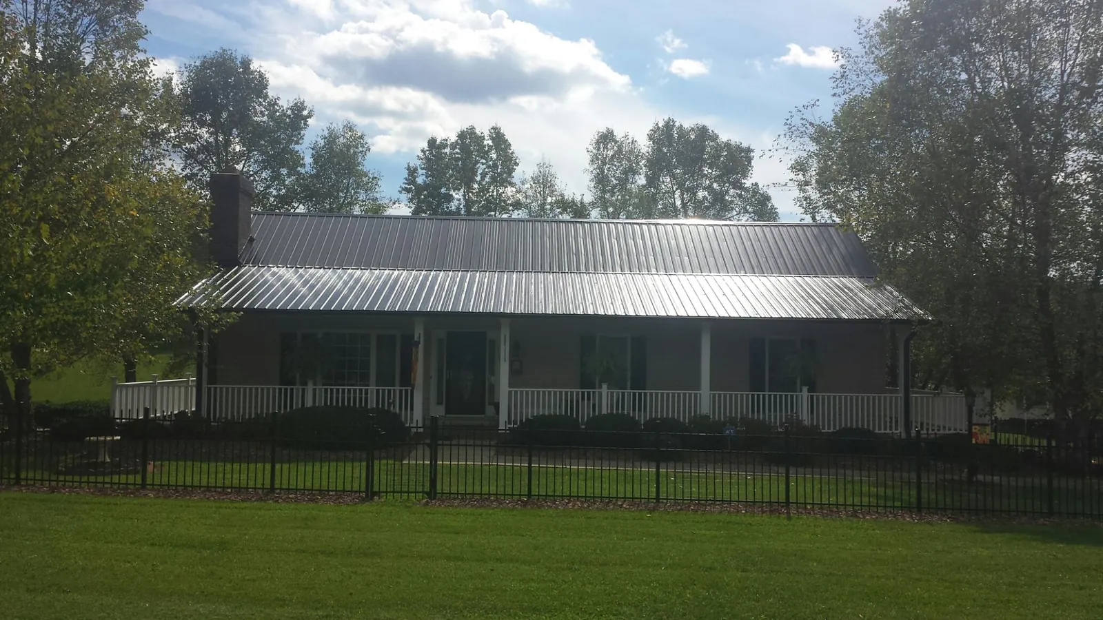 Gray metal roof on a brick ranch with a full width front porch — Gutter Guard Installation work by our crew in Blue Springs