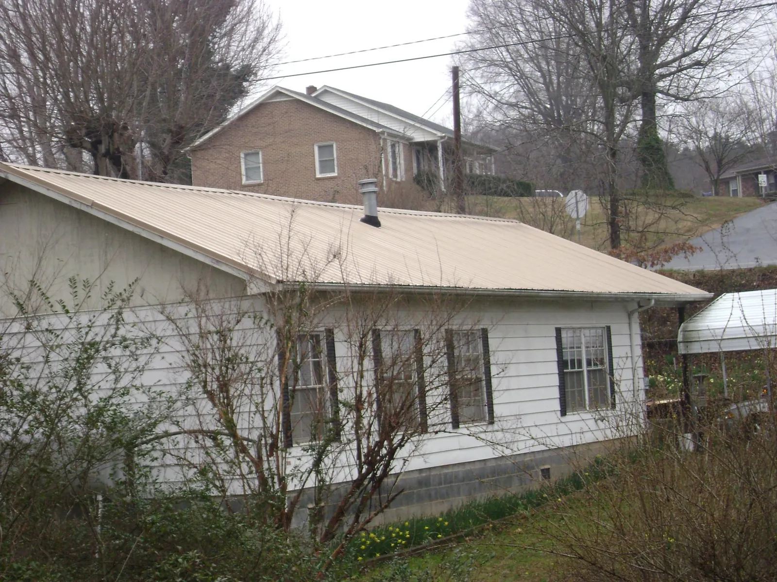 Tan metal roof on a white sided house set into a hillside — Commercial Roofing by Roofing Brothers in Blue Springs