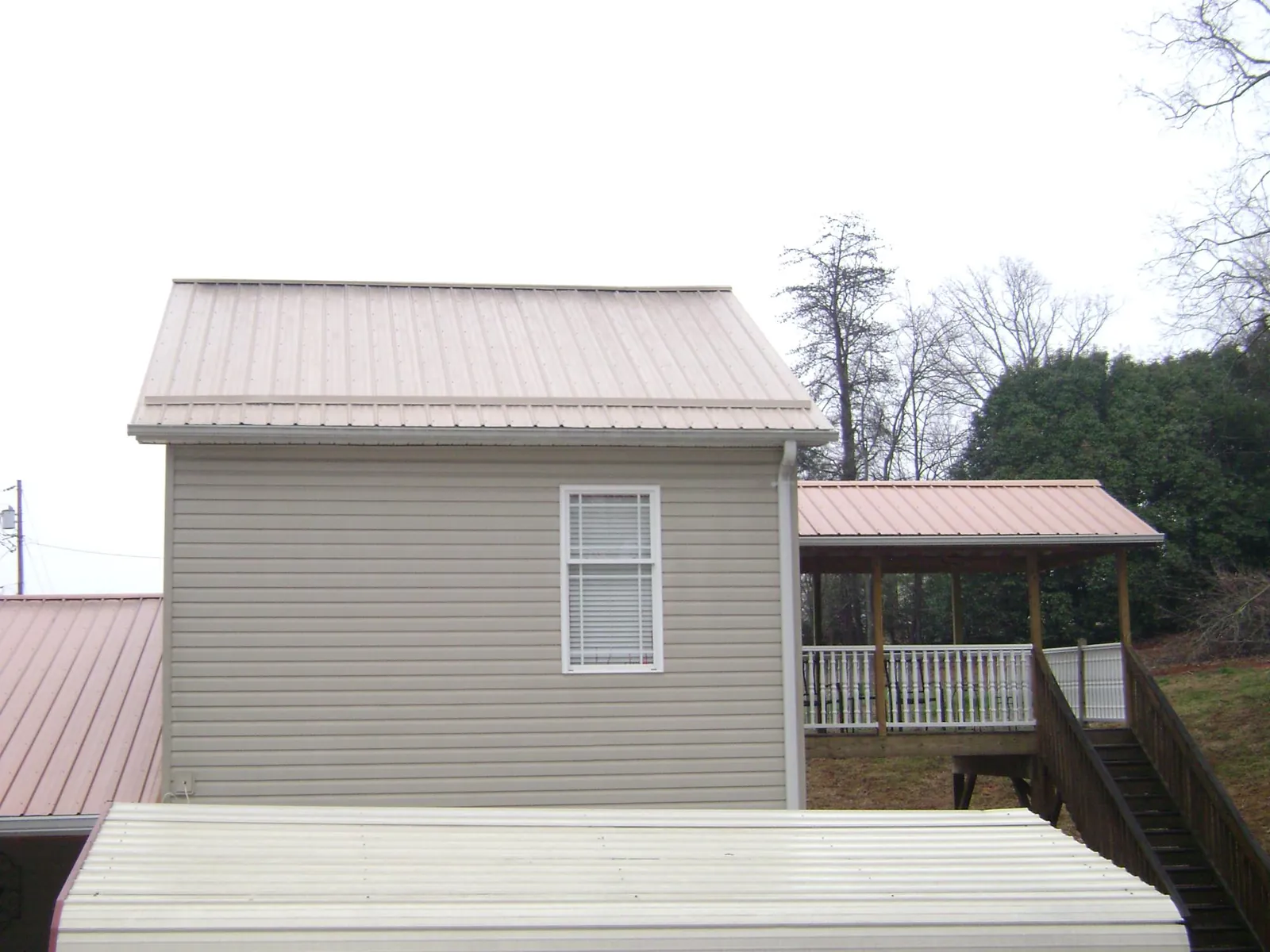 Tan metal roofs on a two story addition and attached porch, from a Roof Replacement job in Blue Springs